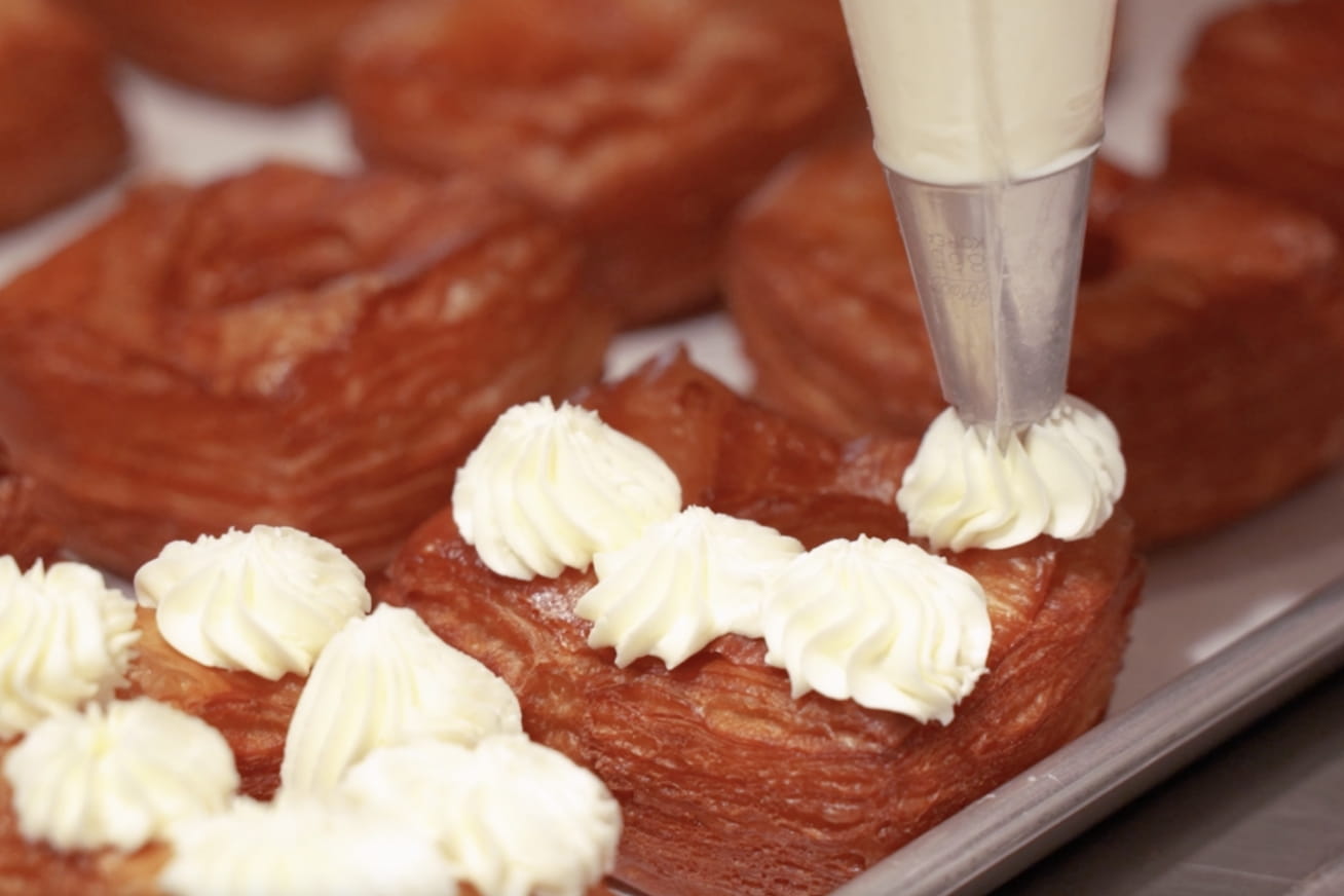 Brioche dough being piped with white cream filling using a pastry bag